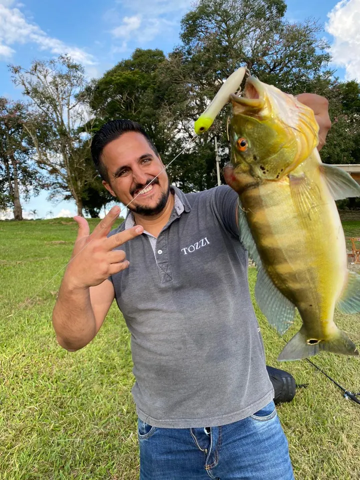 Pescador com um tucunaré amarelo fisgado na isca artificial